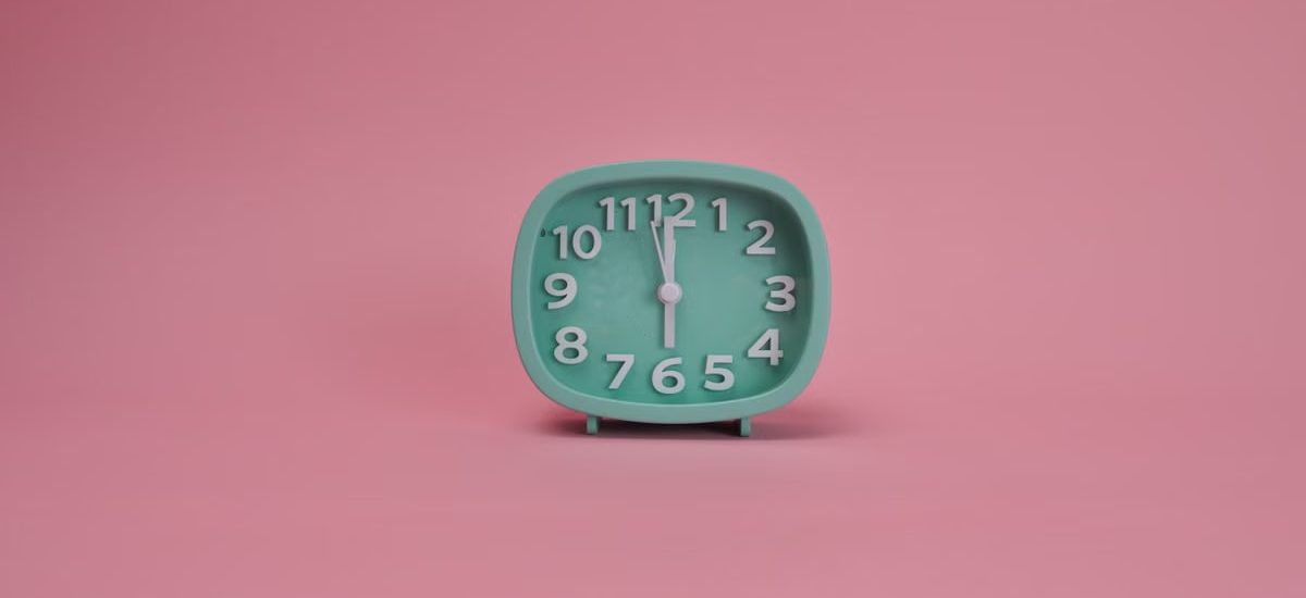 A teal alarm clock against a pastel pink background indicating a minimalist style.