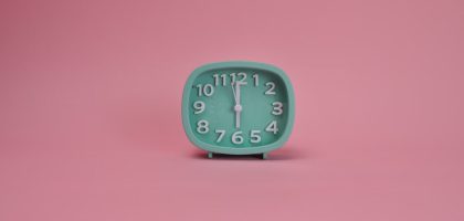 A teal alarm clock against a pastel pink background indicating a minimalist style.