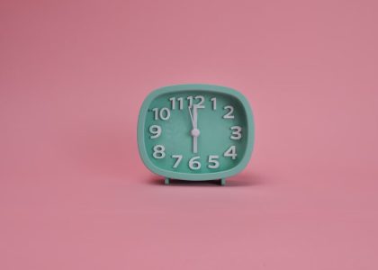 A teal alarm clock against a pastel pink background indicating a minimalist style.