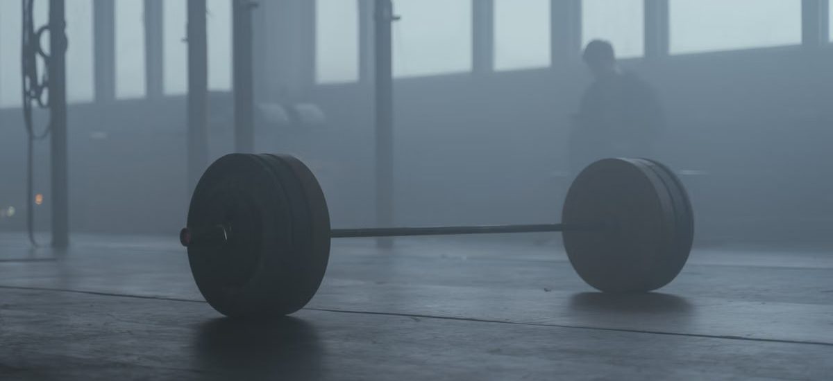A lone barbell on the gym floor with a misty background creates a mysterious and moody ambiance.