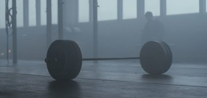 A lone barbell on the gym floor with a misty background creates a mysterious and moody ambiance.